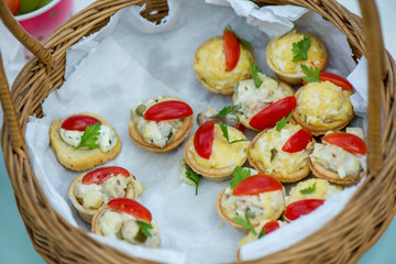 Cheese snacks with tomato slices and herbs in wooden basket. Leftovers from birthday celebration