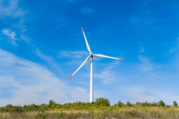 Fototapeta premium Rotating windmill generating renewable energy wind power at land. Sustainability by windmills turbines preventing climate change with regenerative clean green nature energy. Windy blue sky with clouds