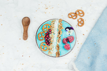 Fresh blue spirulina smoothie bowl with raspberries, pretzels and pomegranate kernels, healthy vegan breakfast concept