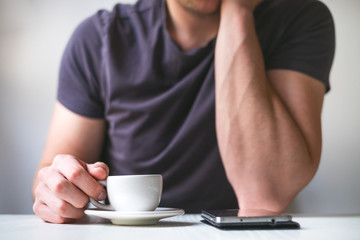 Young man drinking morning coffee and holding mobile phone. Coffee break. Man holding cup of fresh roasted coffee and looking at the smart phone. 