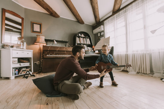 Young father and little daughter playing acoustic guitar