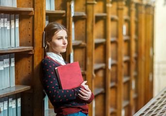 Curious woman standing near library bookshelves with red book