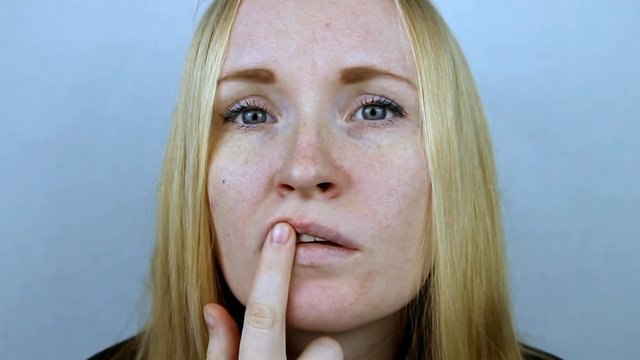 Young beautiful blonde girl looks at the lip on which herpes appeared.