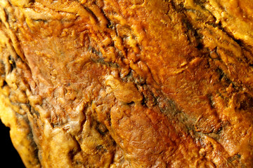 part of the surface of a dried Spanish ham jamon on a black background. background a food of yellow color with a place for an inscription. texture surface of oily pig's foot macro shot