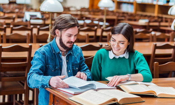 Two smart students working on home assignment, reading books attentively, sitting at square library table in the reading hall
