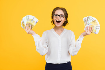 Portrait of confident beautiful happy young business woman with money in her hands standing on yellow background