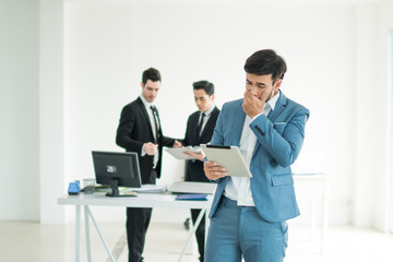 Fototapeta na wymiar Portrait of business man holding tablet and feeling failed, sad, distraught, frustrated while team mates discussing in the background