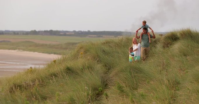 Wide angle, slow motion, of a family walking through the sand dunes while on holiday in Northumberland.