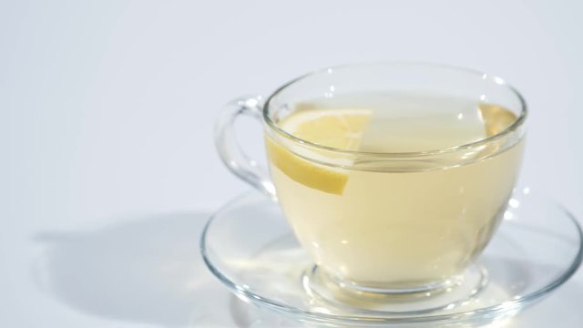 In a cup on a saucer with black tea falls a slice of lemon on a white background, slow mo