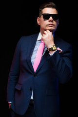 Portrait of confident handsome businessman in sunglasses holding hand near beard on black background