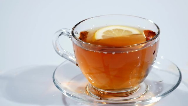 In a cup on a saucer with black tea falls a slice of lemon on a white background, slow mo