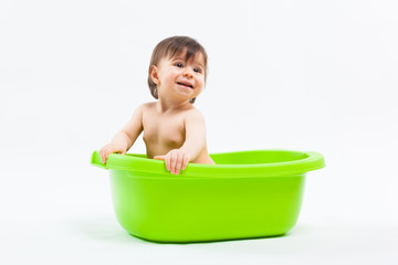 Adorable caucasian smiling girl taking bath in green tub on white background