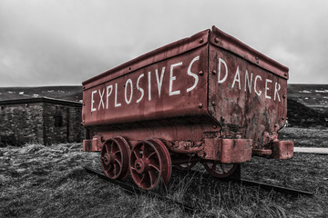 Fototapeta na wymiar A bright red, weathered, mine cart, used to carry explosives to the Welsh coal mines. The cart is located in the Big Pit, tourist attraction in Ebbw Vale, in the South Wales Valleys