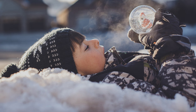 Side view of boy with snow globe lying outdoors during winter