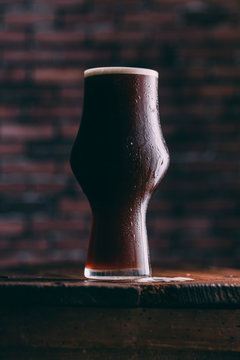 Stout beer glass on wooden table against brick wall