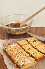 Top view of three rows of freshly baked apricot pecan power bars cooling on parchment paper  with a bowl of raw dough and a knife on a wood cutting board