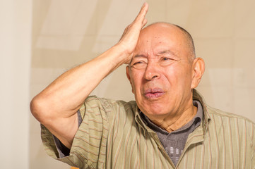 Obraz premium Portrait of a worry mature man touching his head with one hand, in a blurred background