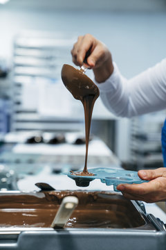 Cropped hands of baker pouring chocolate in mold at factory