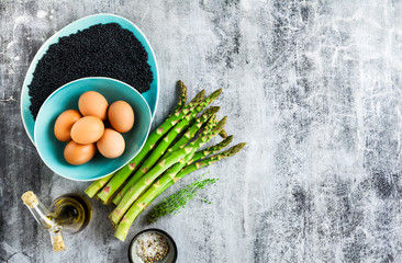 ingredients for cooking asparagus, black lentils, olive oil and eggs on the table on grey stone 