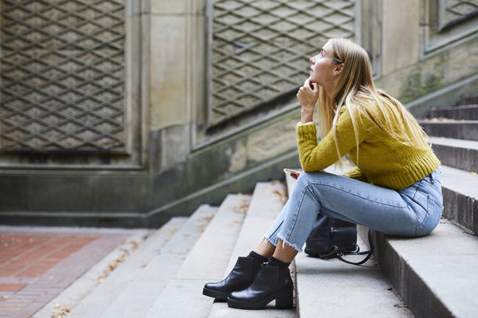 Thoughtful young woman sitting on steps outdoors