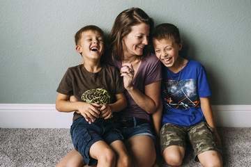 Cheerful mother and sons sitting against wall at home