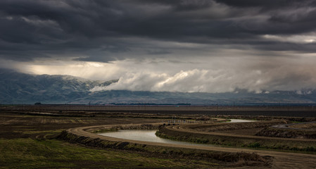 Dramatic stormy skies over Sierra Nevada Foothills with agriculture and irrigation canal