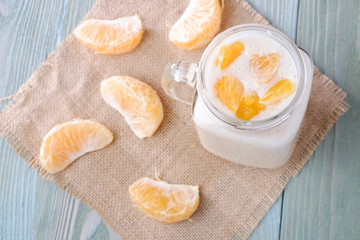 Smoothies of banana and mandarin in a glass cup, mandarin slices, on a wooden table