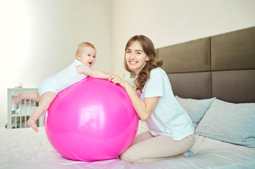 Mother with the baby on the pilates ball on the bed in the bedroom.