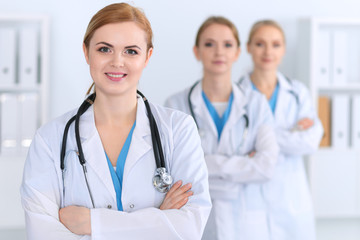 Fototapeta premium Beautiful female medical doctor standing at hospital in front of medical group. Physician is ready to help patients. Medicine and health care concept