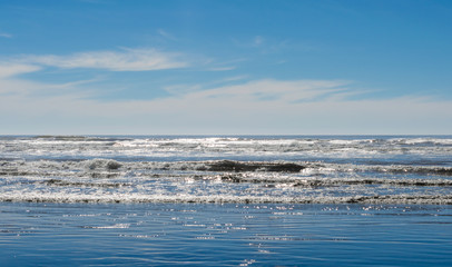 Ocean beach waves splashing onto seaside shoreline. Beautiful seascape, landscape with water and blue skies. 