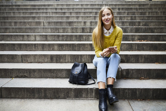 Portrait of young woman holding smartphone while sitting on stairs