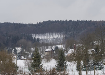 winter view on village travnik with chapel, cottage and trees, snow covered rural landscape with spruce tree forest in luzicke hory mountain
