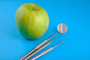 Green apple and metal dental instruments on a blue background