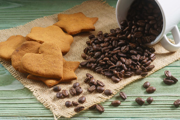 White porcelain cup, scattered coffee beans, homemade cookies on a wooden table, close-up