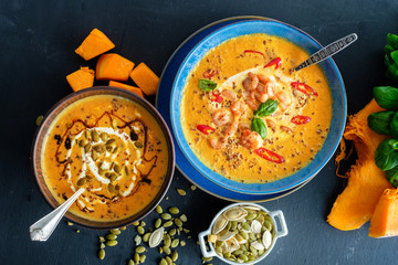 Delicious homemade pumpkin soup with prawns, chili and basil leaves. Top view.