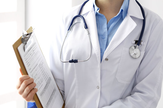 Female doctor filling up medical form on clipboard closeup.  Physician finishing up examining his patient in hospital and ready to give a prescription to help. Healthcare, insurance and medicin