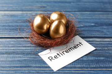 Golden eggs in nest and sign RETIREMENT on wooden background. Pension planning