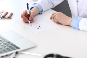 Female doctor filling up prescription form while sitting at the desk in hospital closeup.  Physician finishing up examining his patient in hospital and ready to give an advice to help. Healthcar
