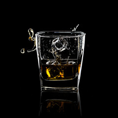 Glass of splashing whiskey isolated on black