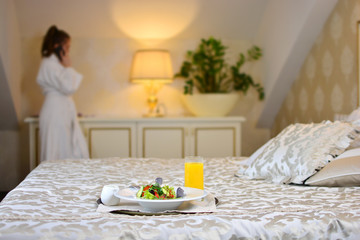 Breakfast in a bedroom of a luxury resort. Girl speaks phone on a background.