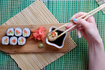 The girl is holding chopsticks ready to roll and dipping it into soy sauce, top view