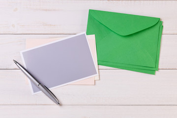 Top View of a invitation or Letter with a Green Envelope. Message or Ticket on Wooden White Desk or Table. Writing a note. Pen, Pencil, a Blank Notebook. Picture. Copy space for text or Image.