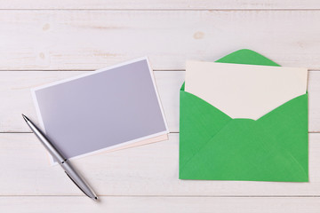 Top View of a invitation or Letter with a Green Envelope. Message or Ticket on Wooden White Desk or Table. Writing a note. Pen, Pencil, a Blank Notebook. Picture. Copy space for text or Image.