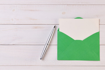 Top View of a invitation or Letter with a Green Envelope. Message or Ticket on Wooden White Desk or Table. Writing a note. Pen, Pencil, a Blank Notebook. Picture. Copy space for text or Image.