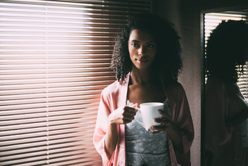 pretty black woman standing at the window with cup of coffee