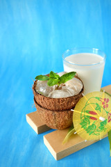 Coconut halves with ice cubes. A glass of coconut milk next to it. Ingredients for a tropical cocktail on blue background
