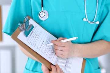 Female doctor filling up medical form on clipboard closeup.  Physician finish up examining his patient in hospital and ready to give a prescription to help. Healthcare, insurance and medicine concept 