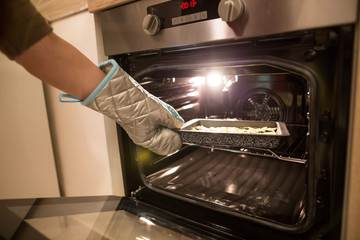 Young woman hand with kitchen gloves putting the food into the heated oven