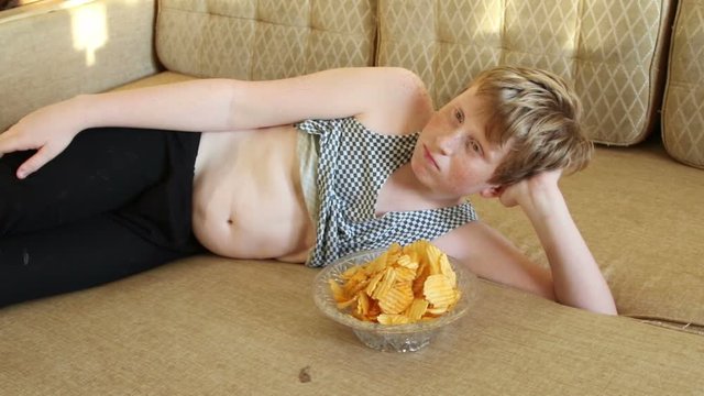 Fat boy eats chips on a sofa
