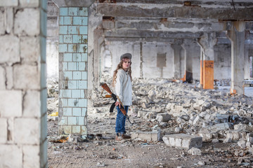 Obraz na płótnie Canvas a little girl alone in an abandoned and ruined building with a Kalashnikov assault rifle and arms making her way to survive